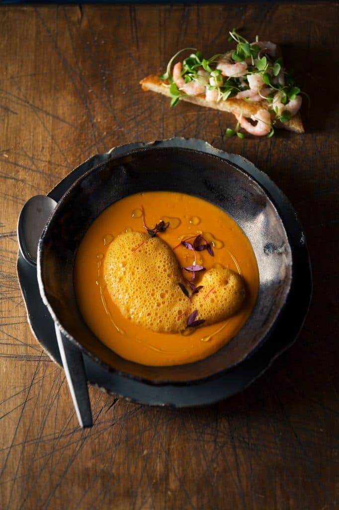 a bowl of carrot soup with a spoon on a wooden table